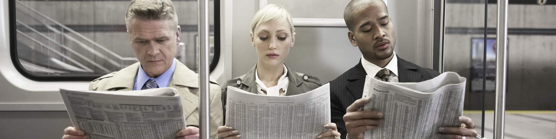 2 Herren und eine Dame sitzen in der U-Bahn und lesen den Finanzteil der Zeitung